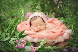 baby girl sleeping in basket in a flower garden