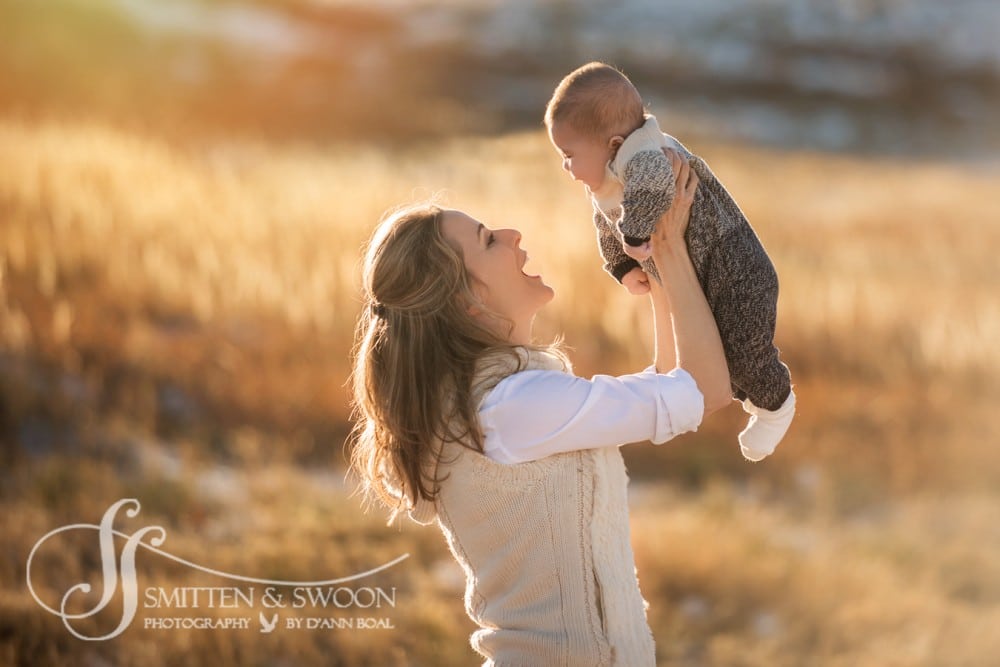 mom lifting baby into the air in golden field