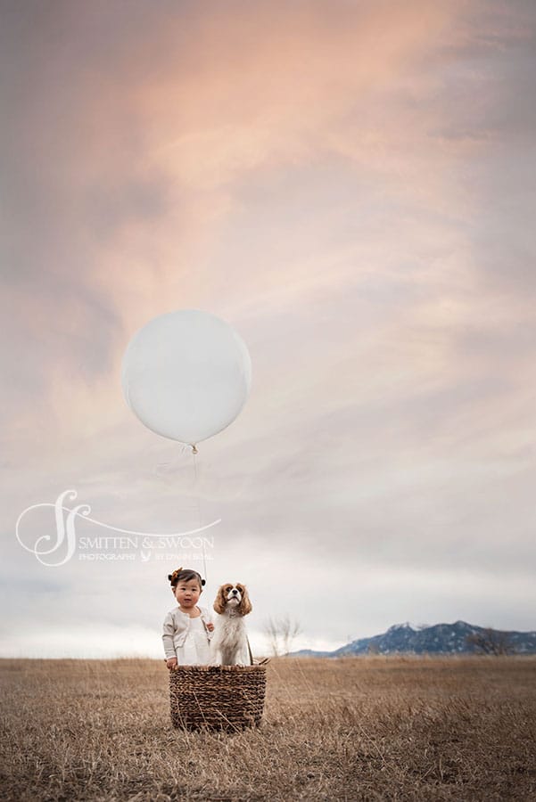 baby girl with her king charles spaniel in a hot air balloon basket with a giant white balloon