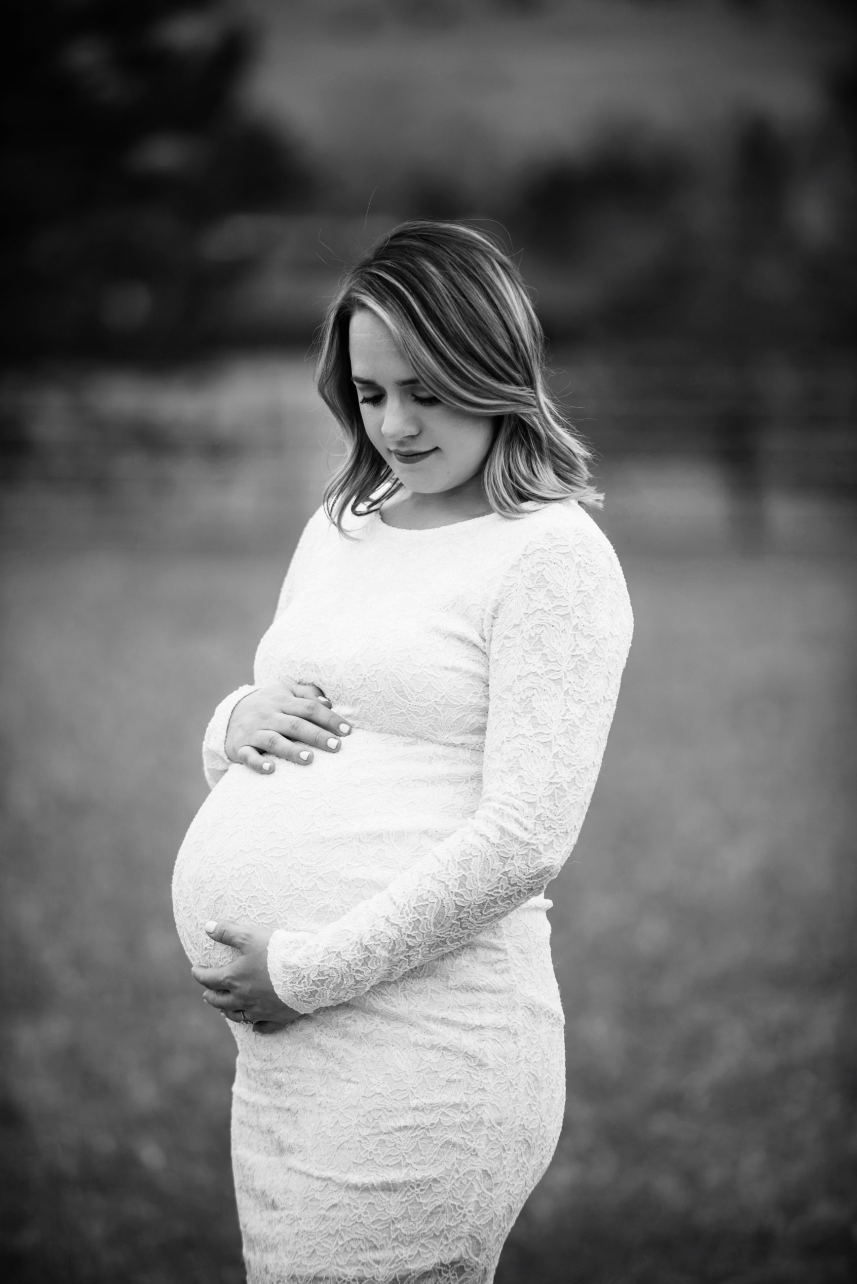 pregnant mother in white lace dress looking down at her belly - maternity photographer boulder