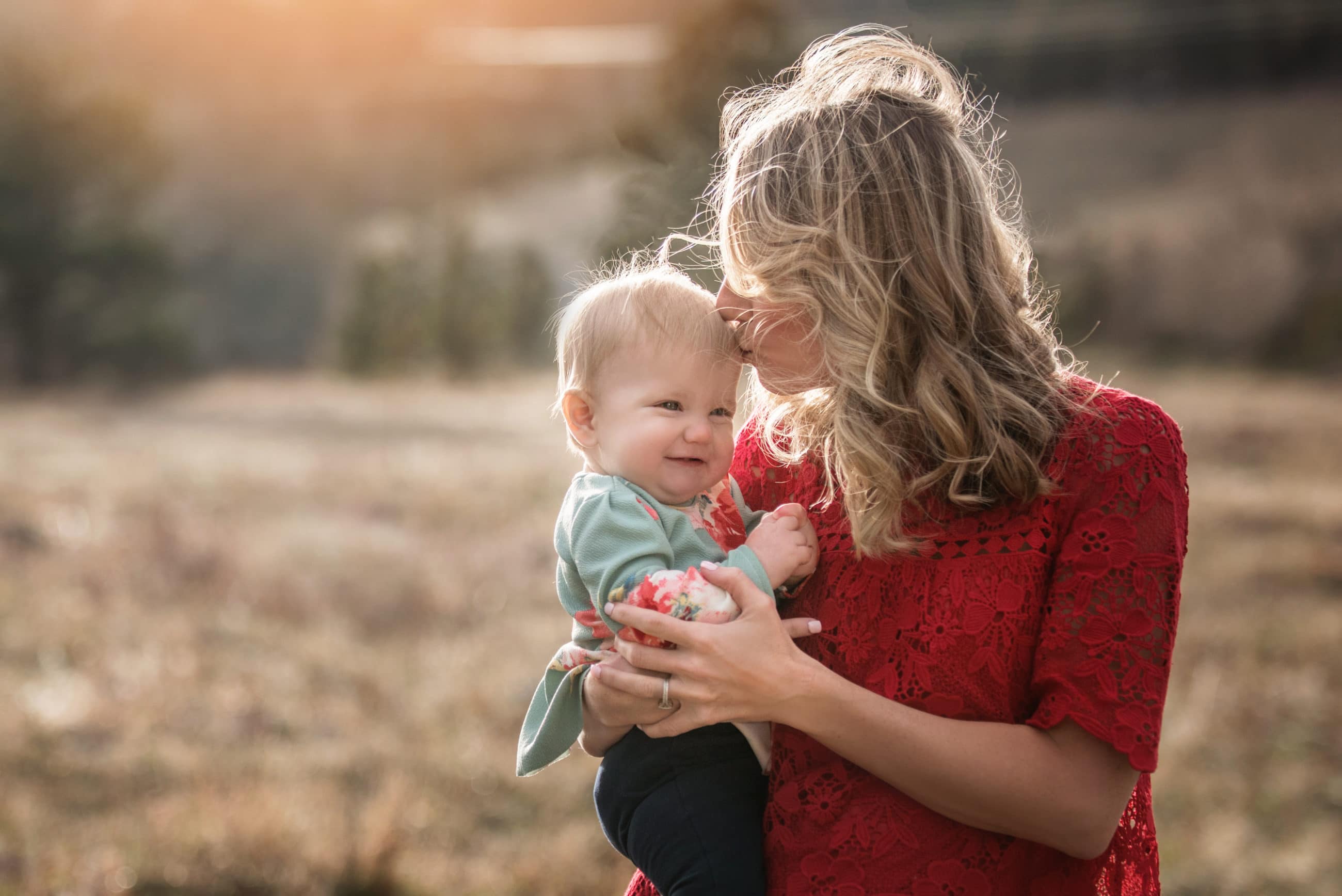 mother wearing red lace kissing her baby girl in golden field - boulder's best photographer