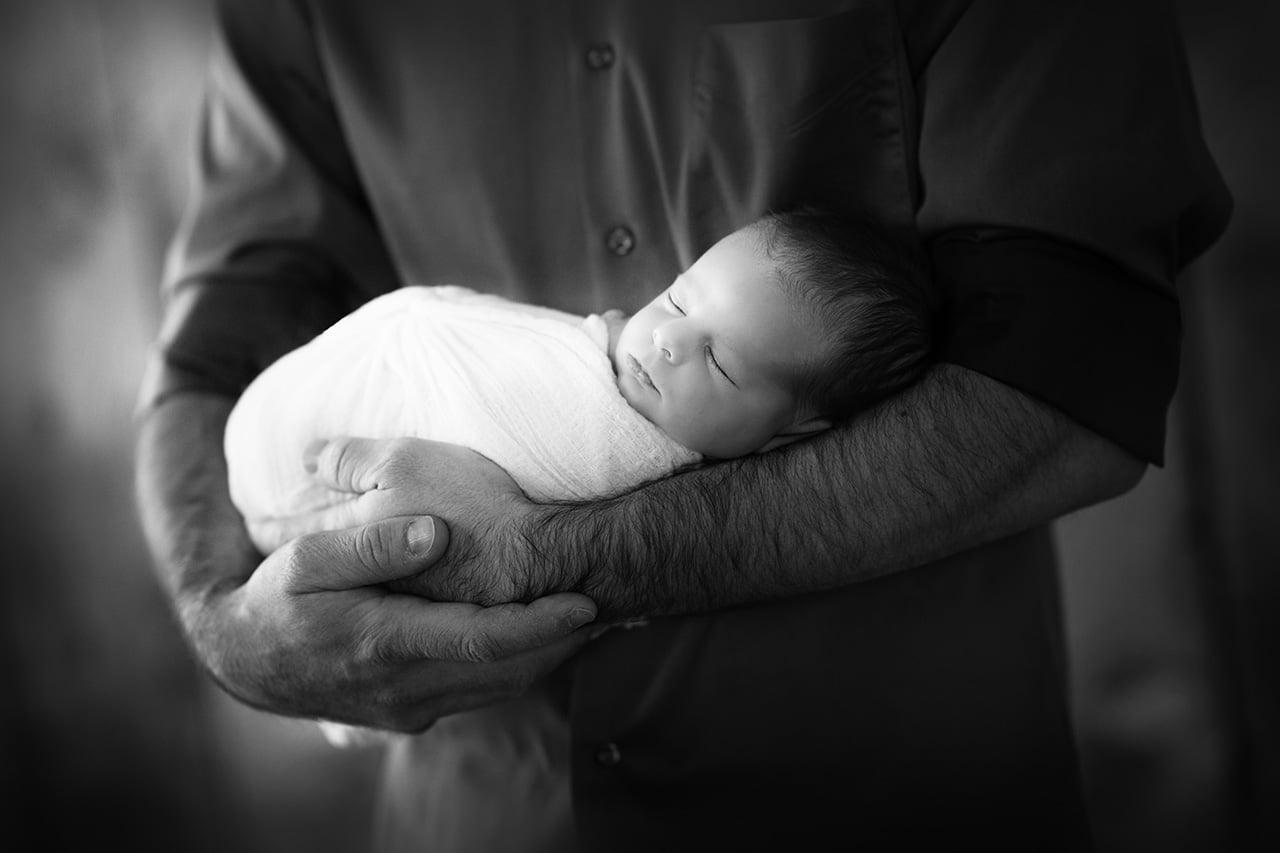 black and white photo of dad holding newborn baby boy wrapped in white sleeping in his arms (boulder photographer)