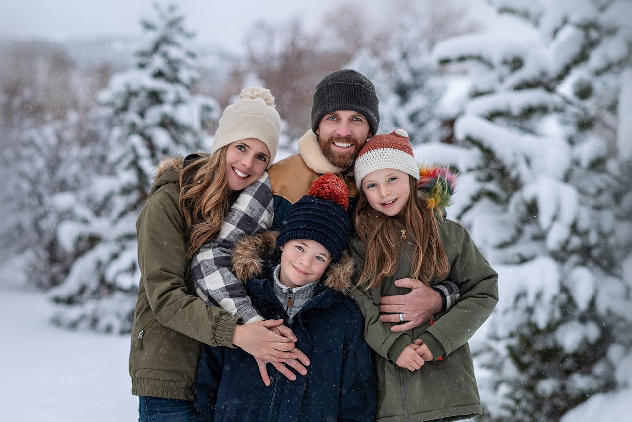winter family photo session family of four smiling with snowy trees in the background (boulder photographer)