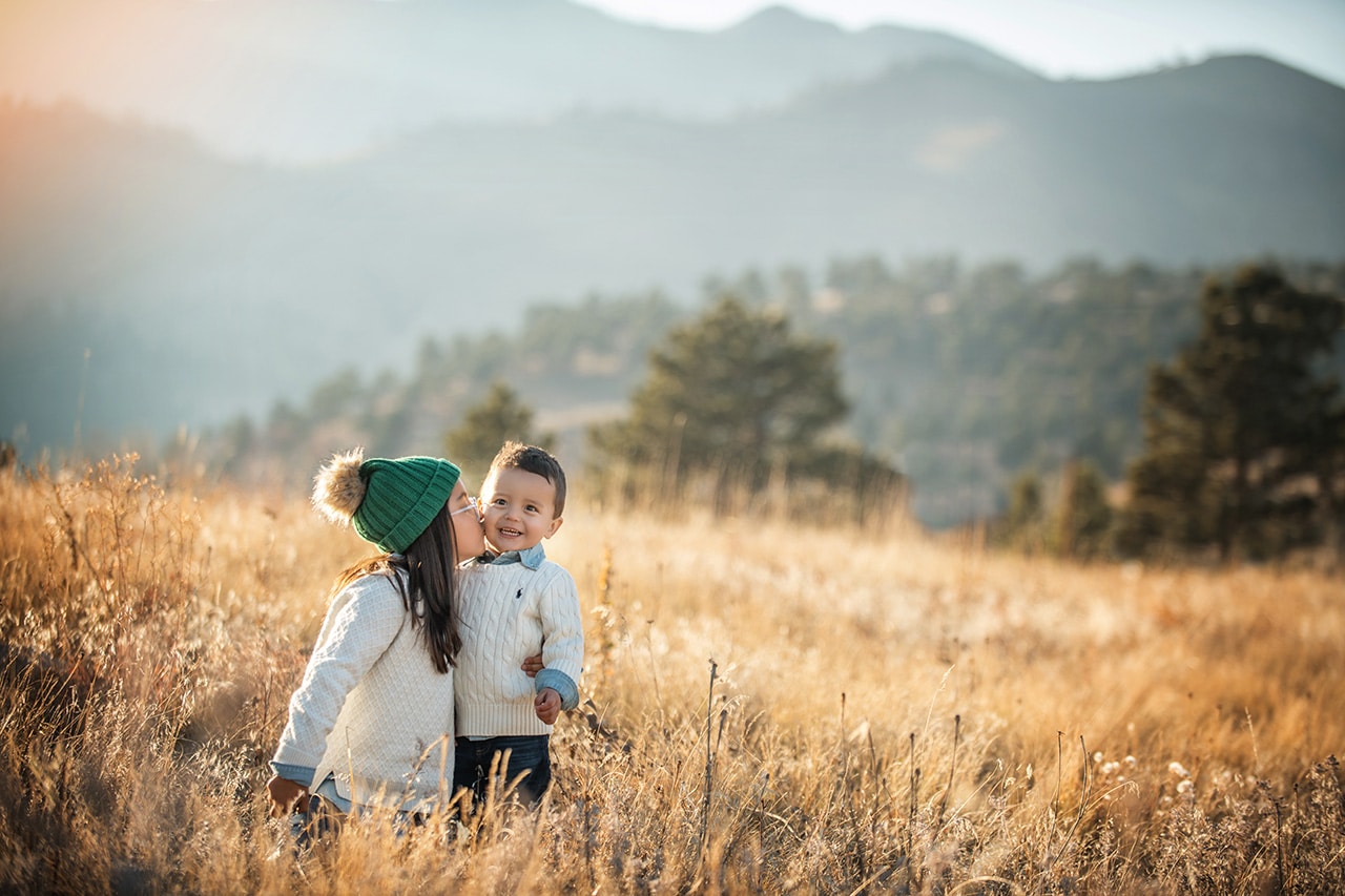 sister kissing brother in golden field with mountains at sunset (boulder photographer)