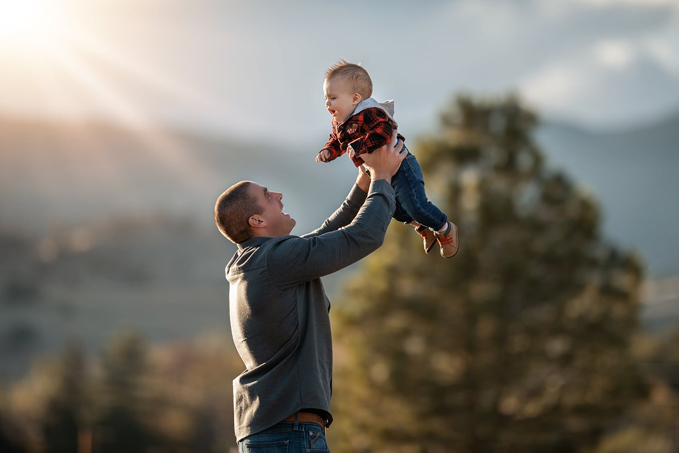 dad holding baby boy up into the air with sun flare and mountains - boulder newborn photographer