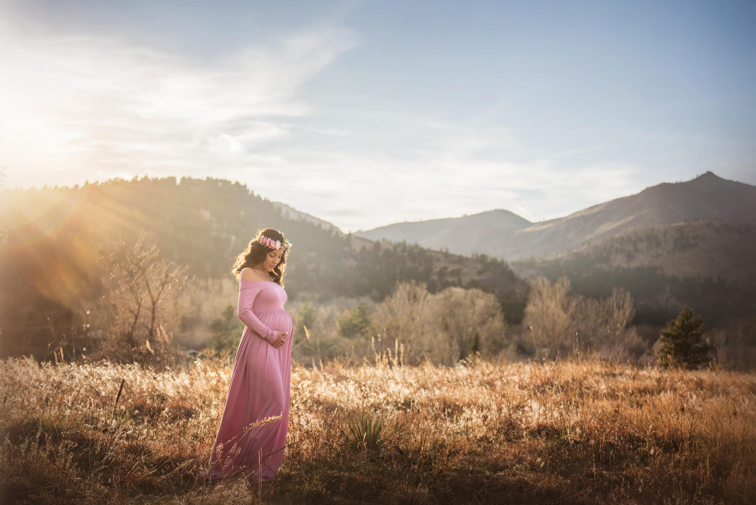 pregnant mom in pink dress in golden field at sunset - baby's first year - boulder newborn photographer