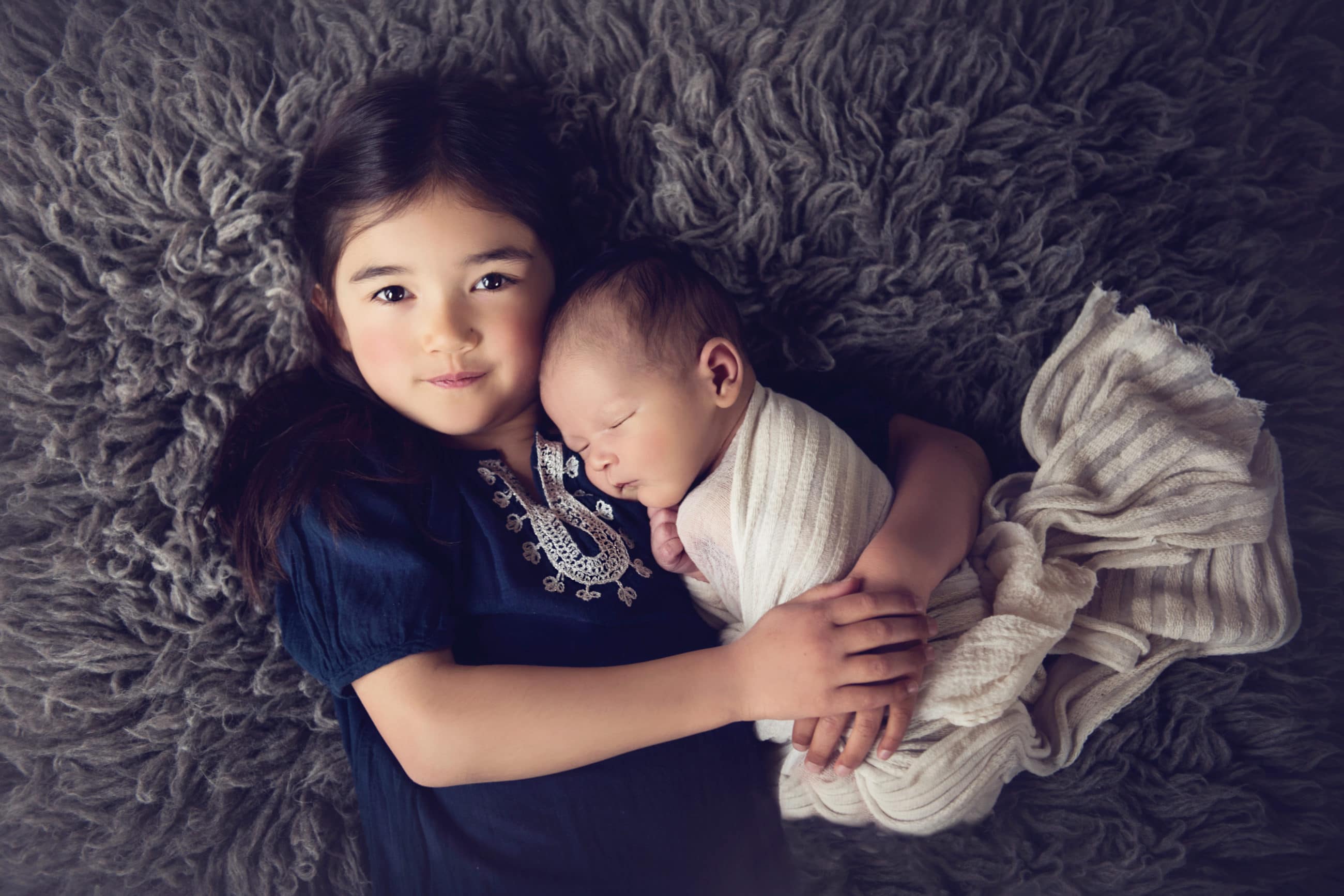 big sister holding newborn baby brother on gray furry blanket - boulder newborn and child photographer