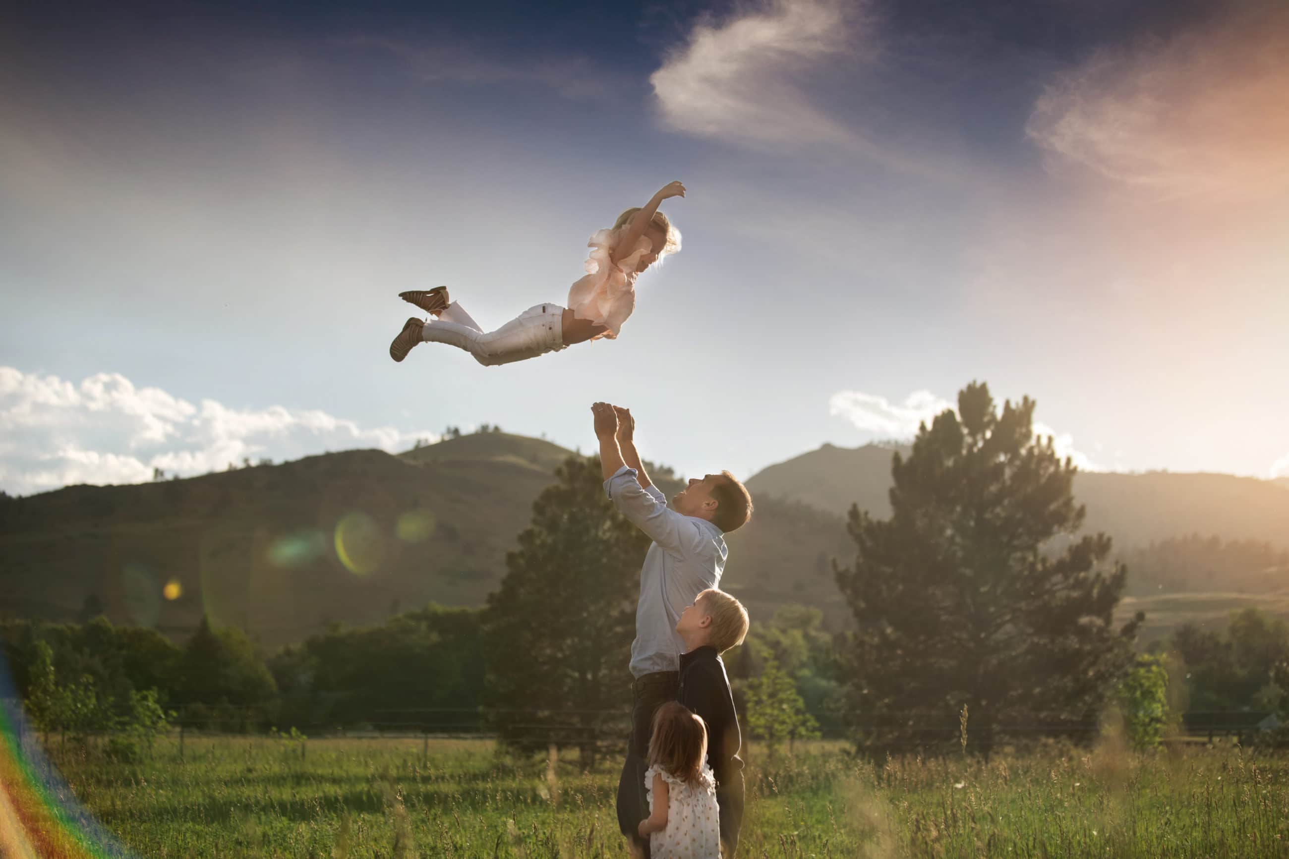 little girl getting thrown into the air with beautiful light and mountains behind her boulder family photographer