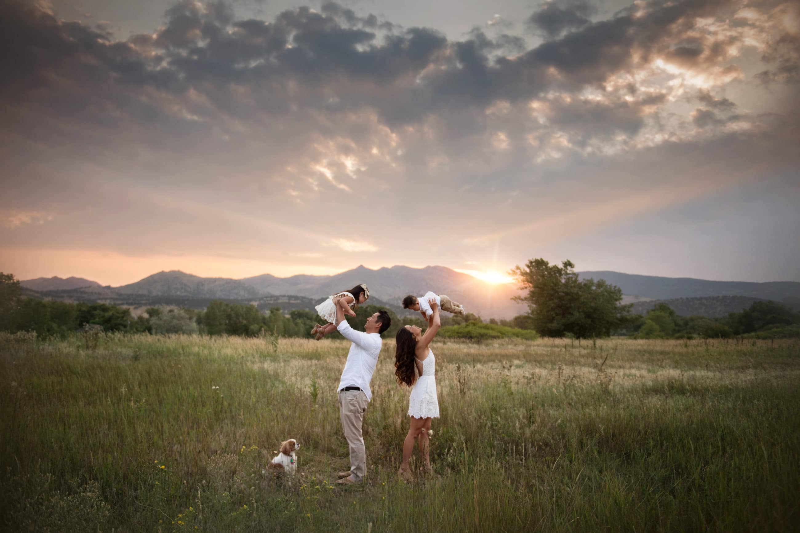 mom and dad holding babies up into the air in field mountains at sunset - boulder family photographer