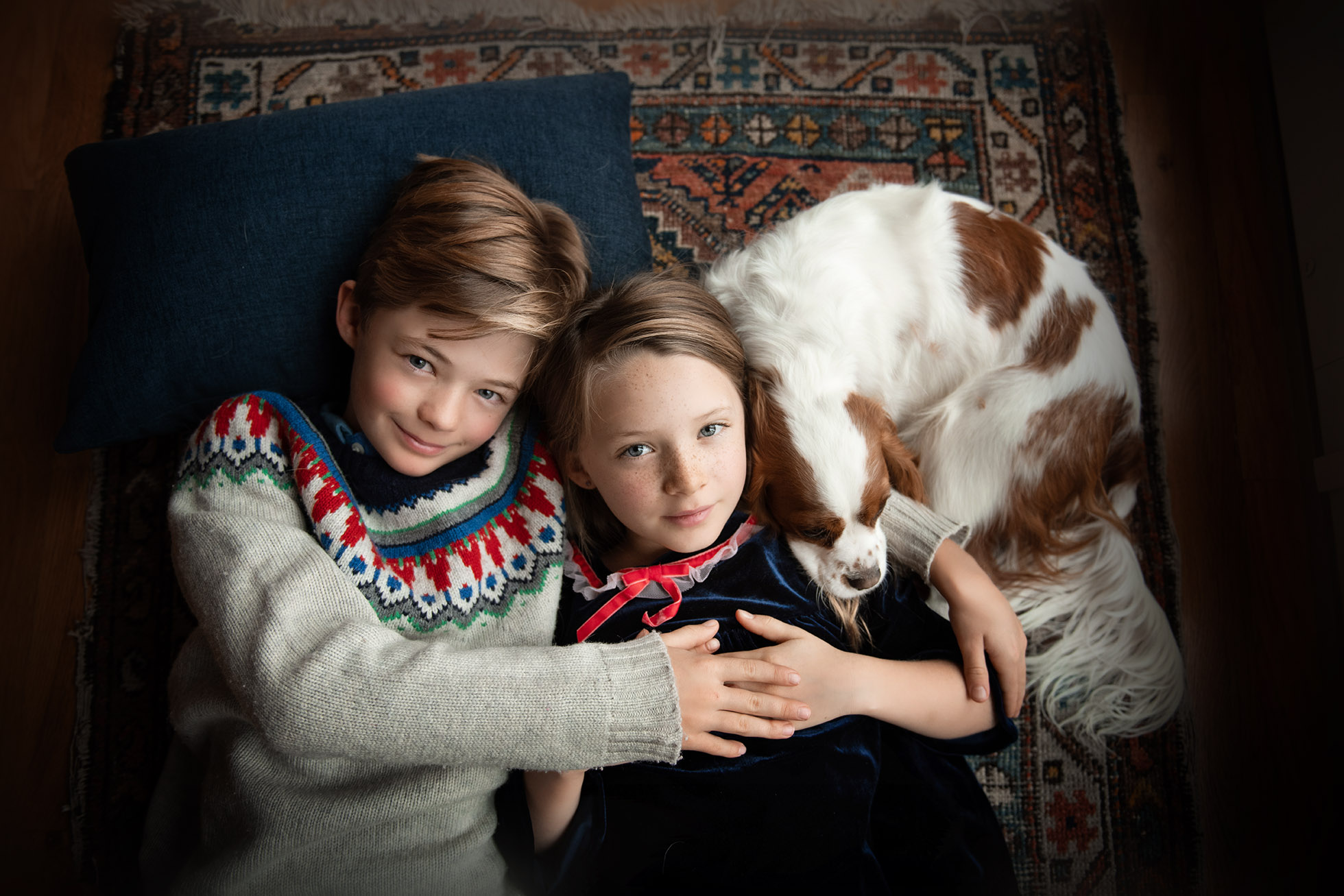 brother and sister hugging on the floor with a cavalier puppy asleep next to them - boulder photographer in home photography