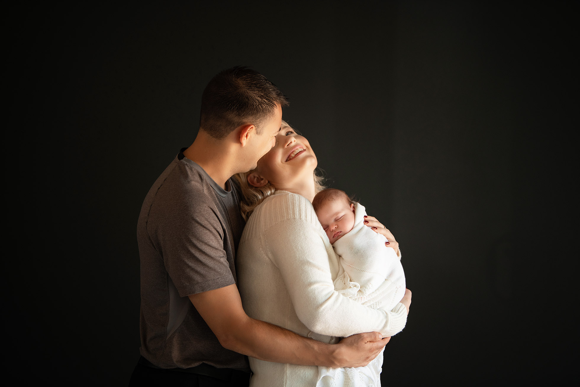 mom and dad laughing holding newborn baby girl in white swaddle - Boulder Photographer | Newborn & Maternity Session