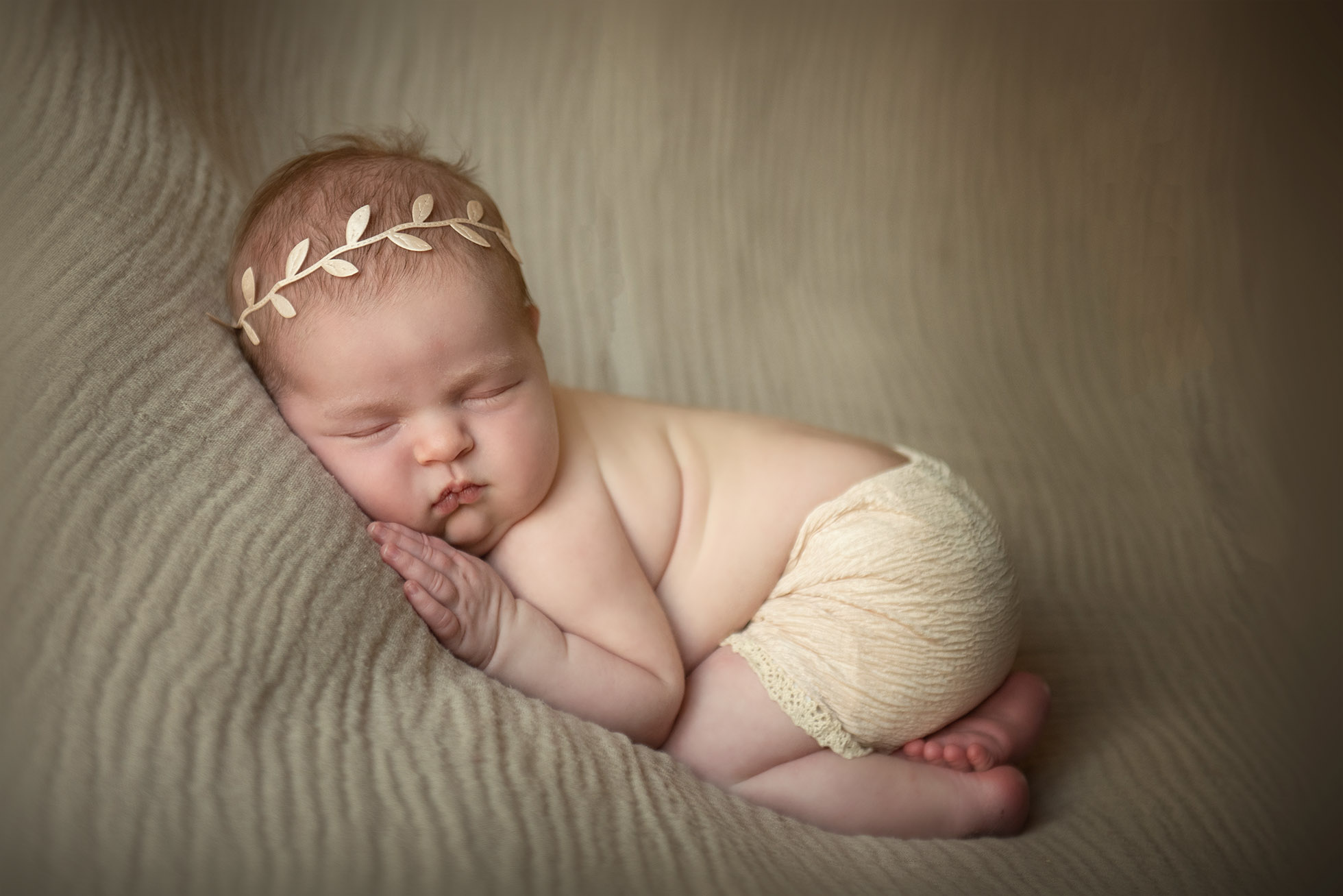 newborn baby girl sleeping on cream blanket knee to elbow pose gold wreath hair band